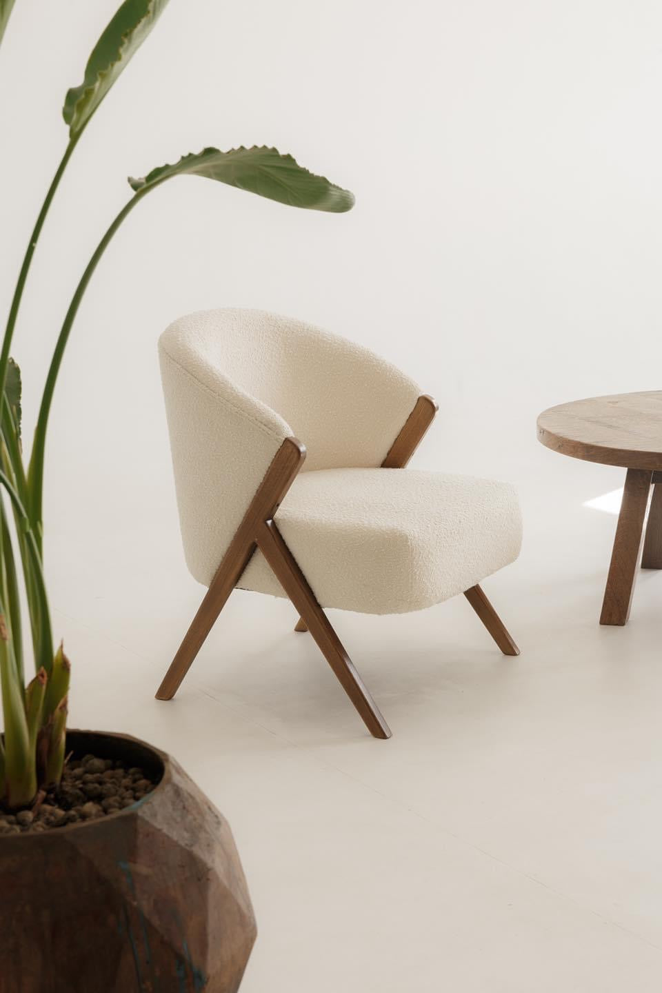 Cozy bouclé armchair with curved silhouette and wooden details – a trendy addition to any space.
