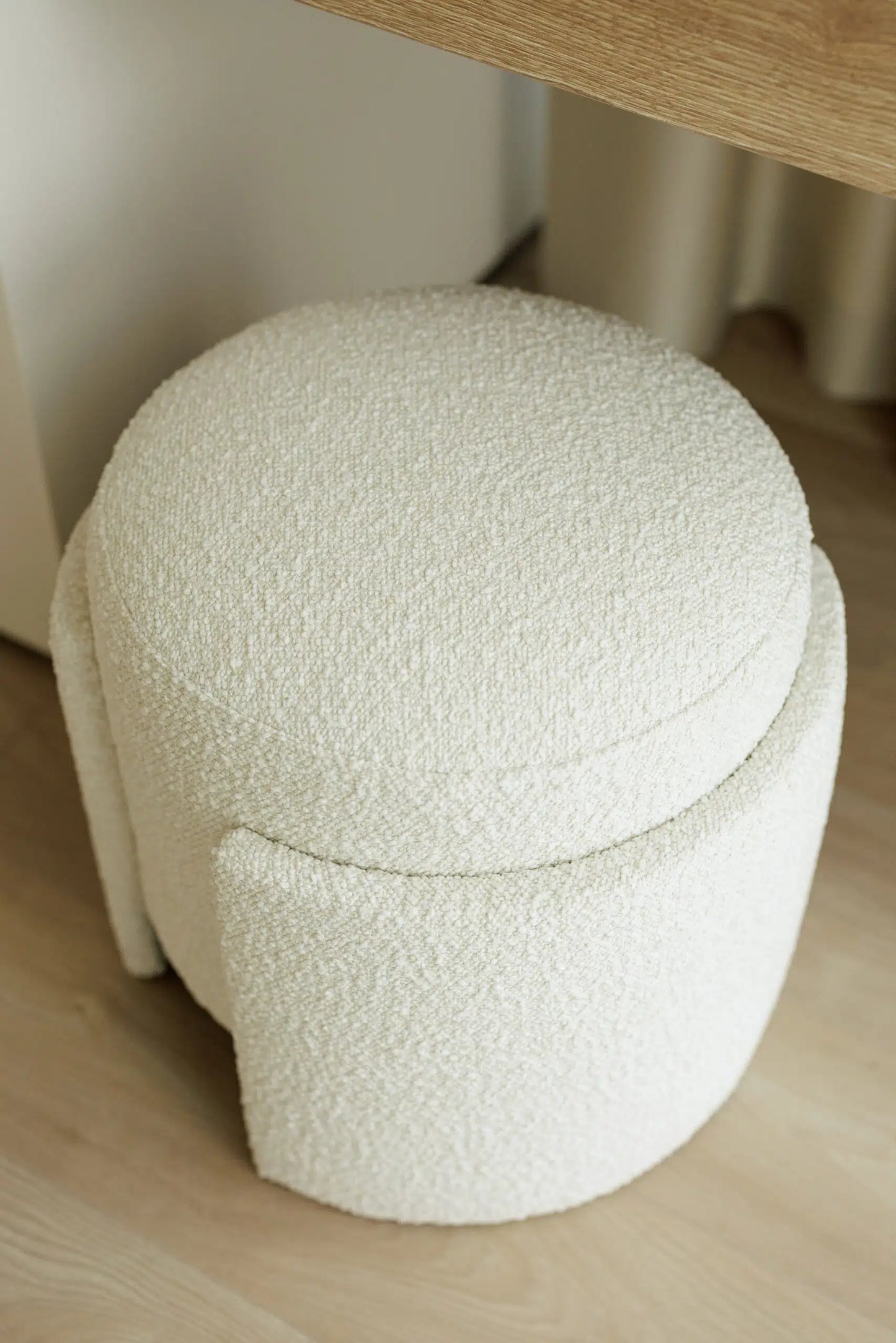 Round white boucle cushioned pouf on a wooden floor