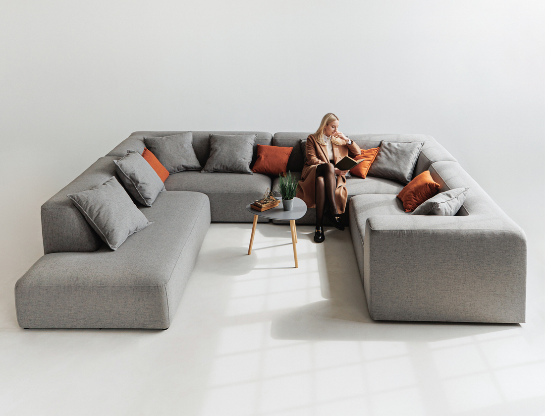 Gray modular sofa in U shape for large living rooms with decorative pillows and model sitting on it. 