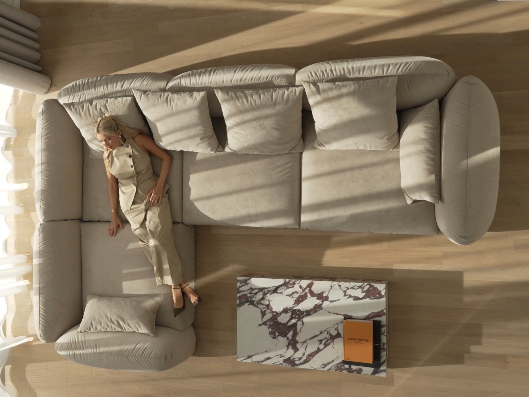 Top-down view of a woman sitting on a large beige sectional sofa in a room with wooden flooring.