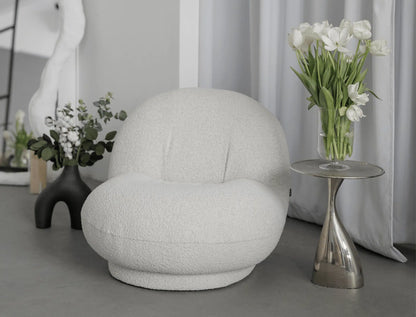 White egg-shaped  boucle armchair in a room with decorative elements including a vase of flowers and a side table.