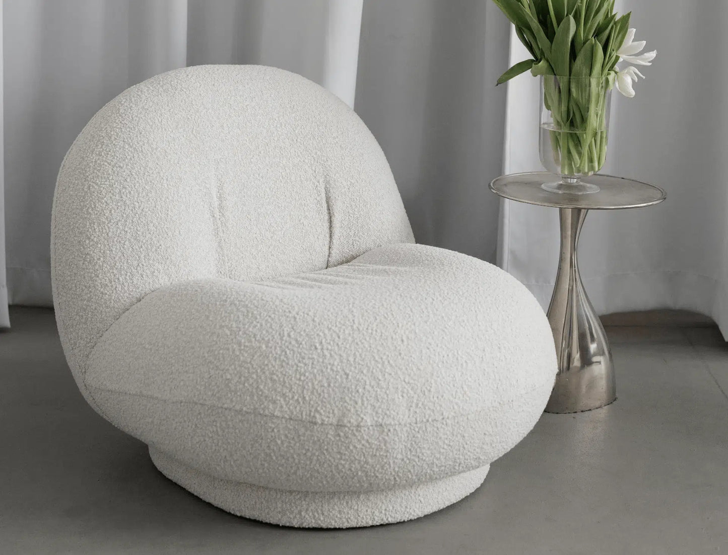 Modern white boucle armchair in a minimalistic room with a side table and flowers.