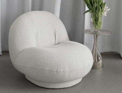 Modern white boucle armchair in a minimalistic room with a side table and flowers.