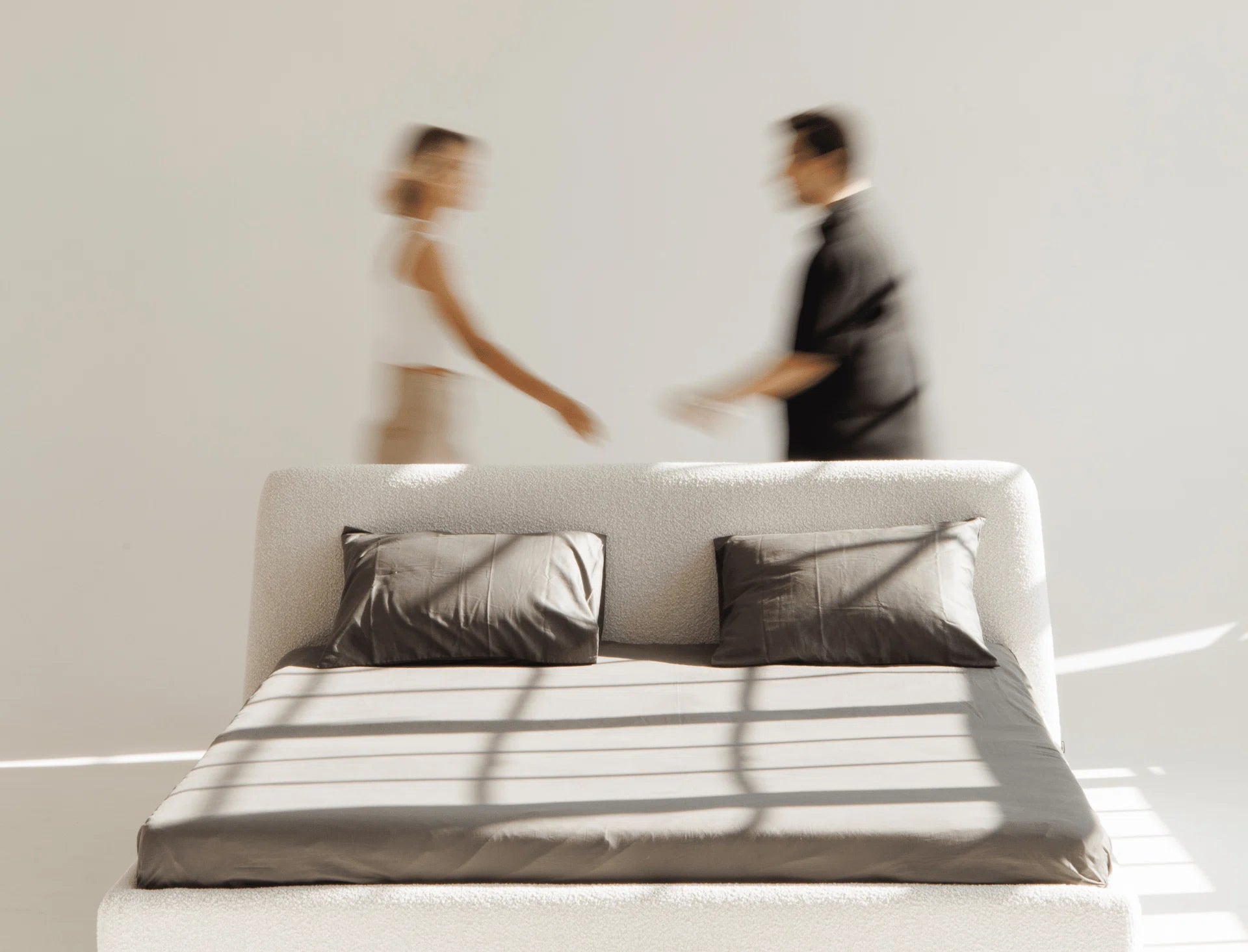 Bed with striped bedding and pillows, blurred figures in the background