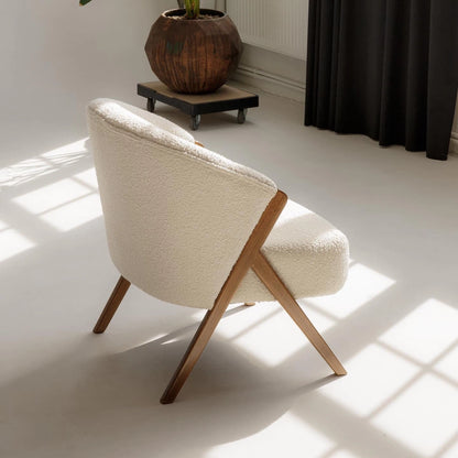 Modern white bouclé armchair with wooden arms next to a plant in a studio. 