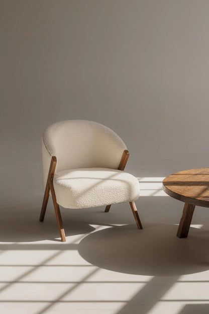 White boucle armchair with wooden legs in a minimalistic room with a wooden table.