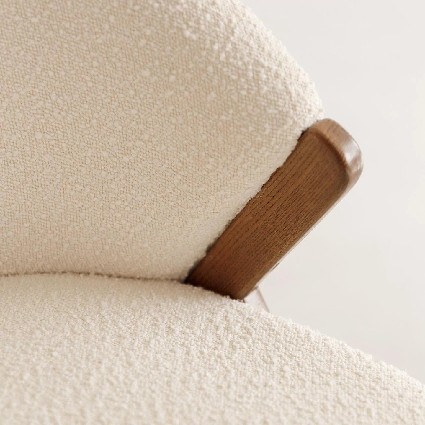 Close-up of a textured beige fabric surface of an armchair with a wooden armrest.
