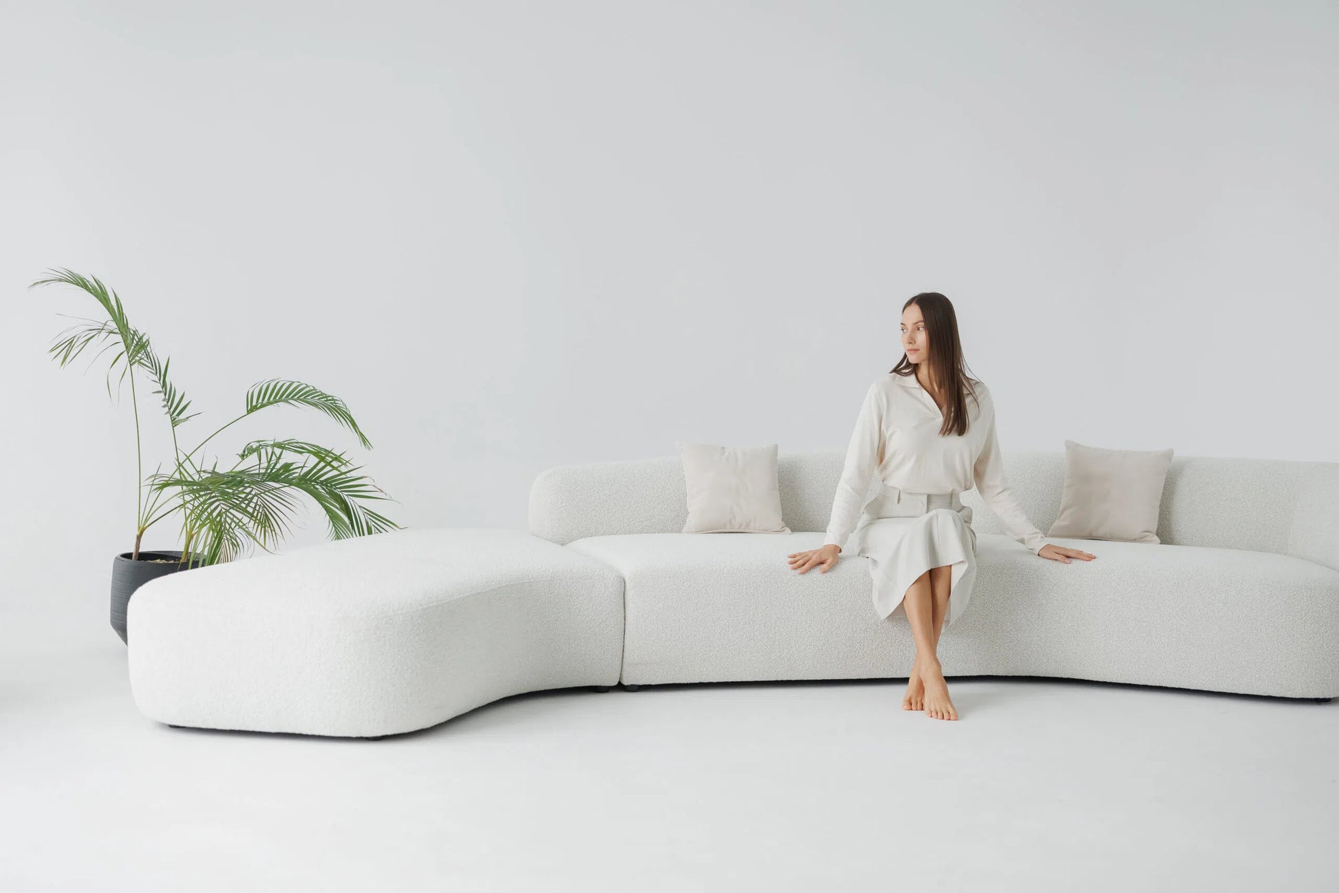 Woman sitting on a modern white teddy sofa in a minimalistic room with a plant.