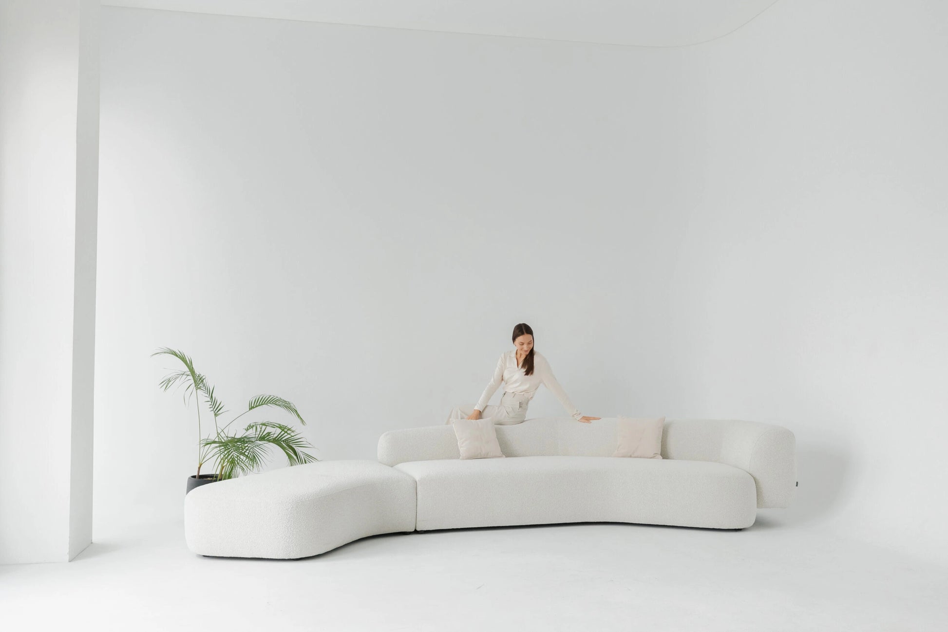 Woman sitting on a modern white boucle sofa in a minimalistic room with a plant.