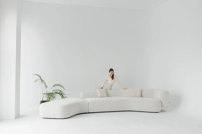 Woman sitting on a modern white boucle sofa in a minimalistic room with a plant.