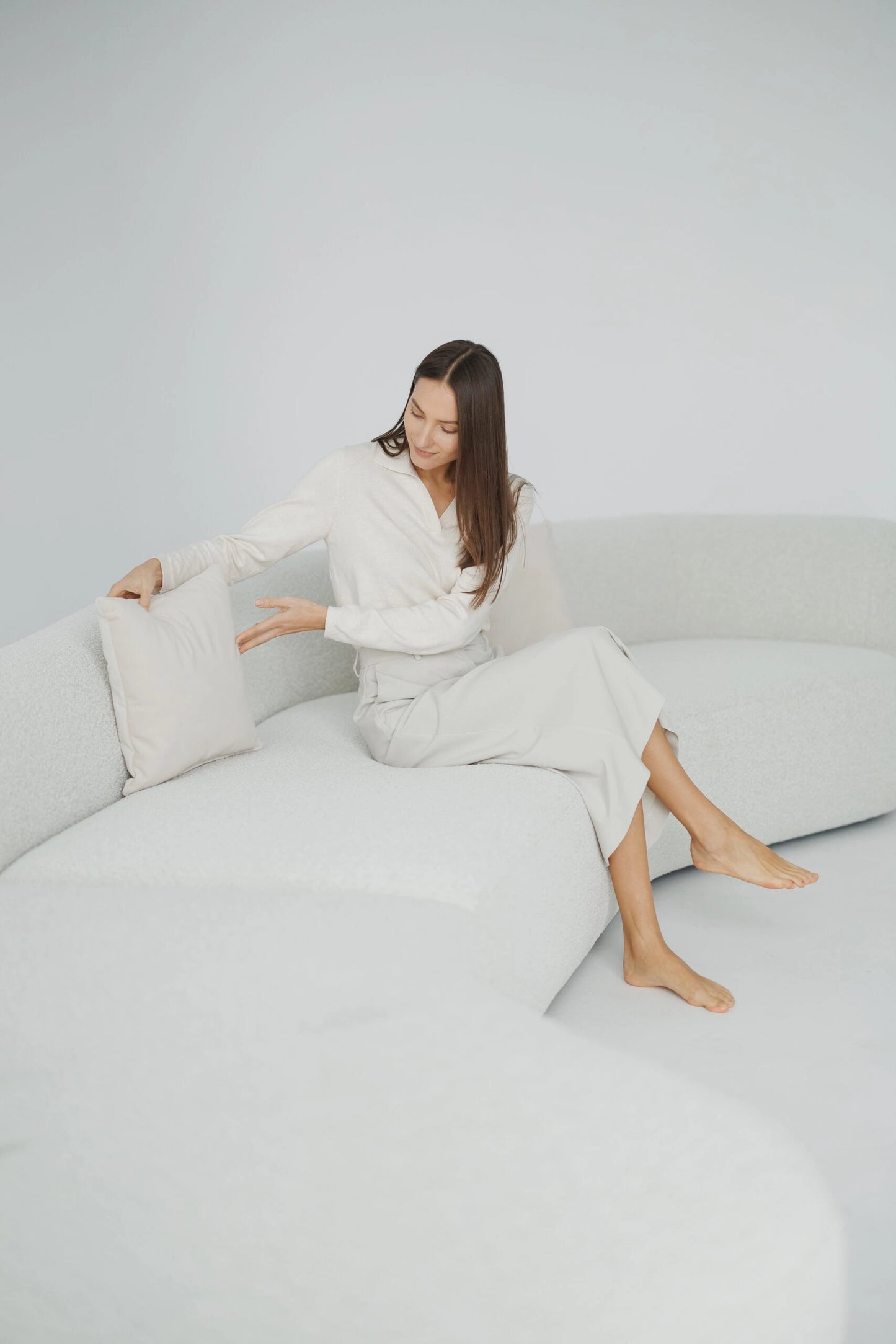 Woman sitting on a white boucle sofas couch with a white pillow.