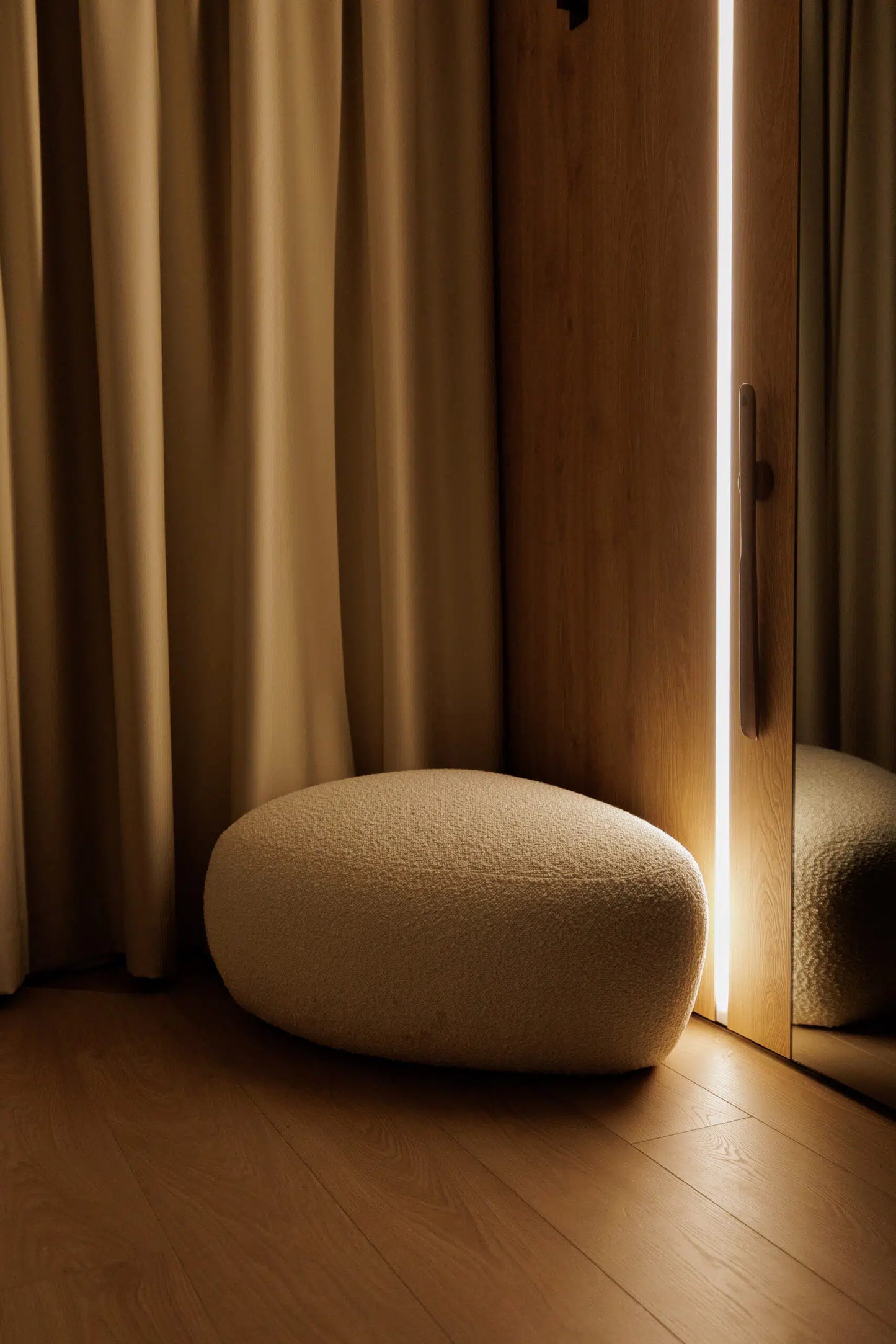 Round beige ottoman in a room with wooden floor and beige curtains