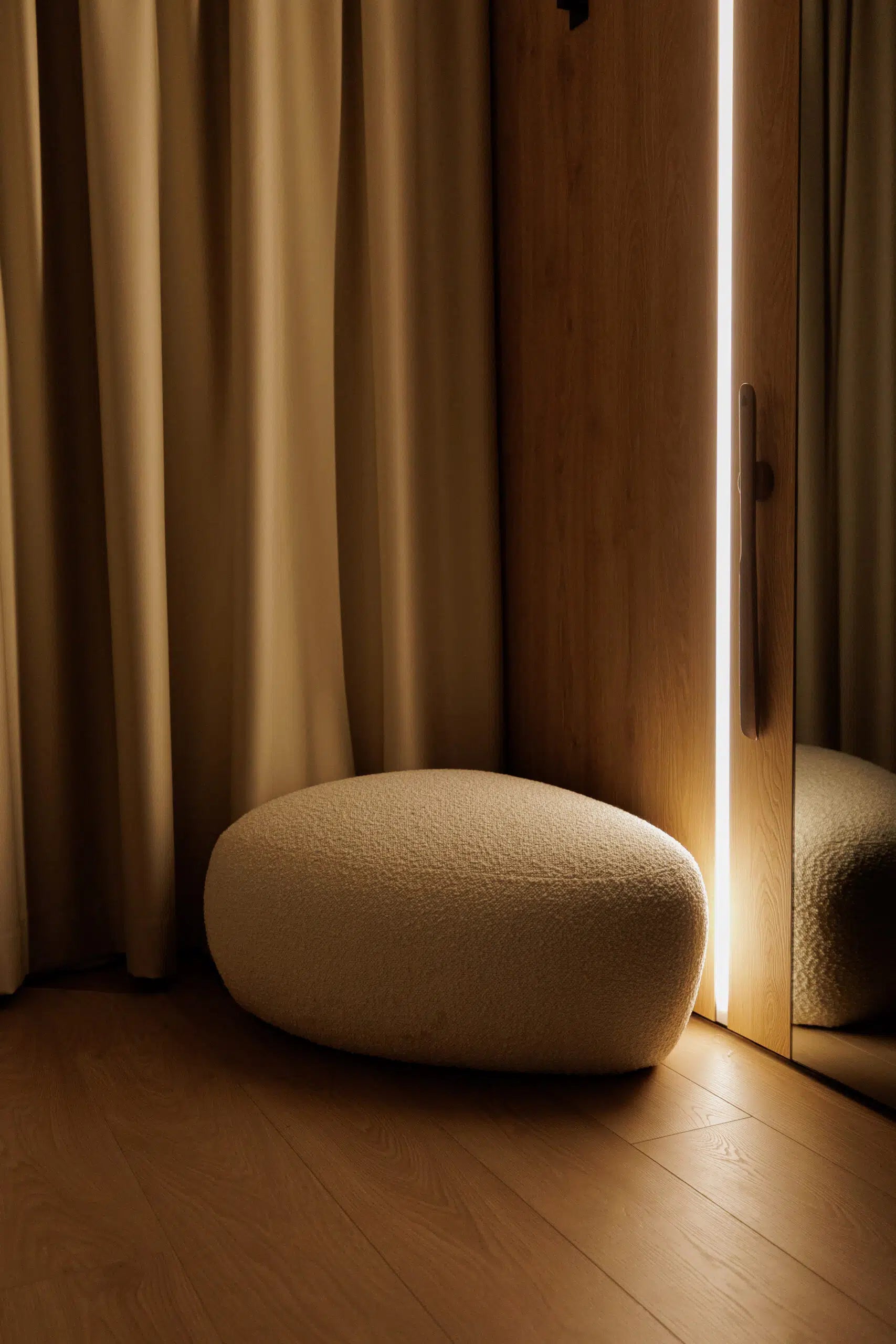 Round beige ottoman in a room with wooden floor and beige curtains