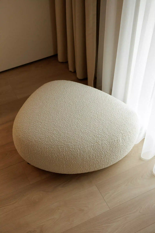 Round textured ottoman on a wooden floor with curtains in the background