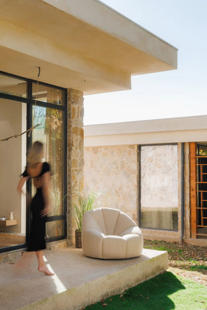 Modern outdoor setting with a beige elegant armchair and a woman in a black dress walking by.