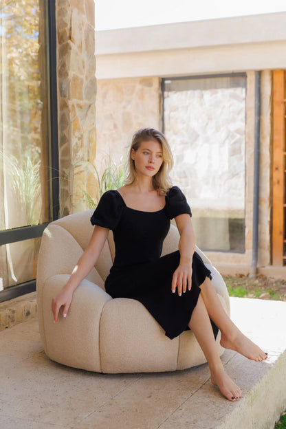 Model in a black dress sitting on a white upholstered armchair in a modern outdoor setting.