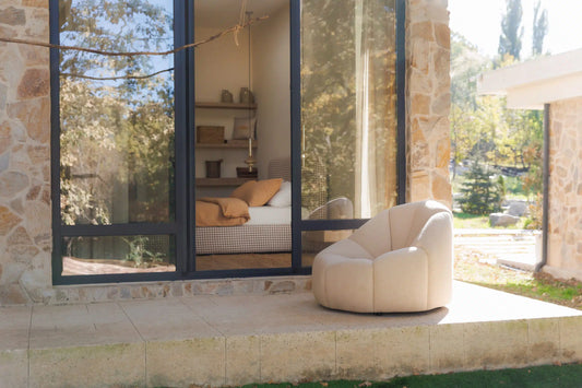 Modern armchair in outdoor seating area with a stone wall and large glass doors leading to a bedroom.