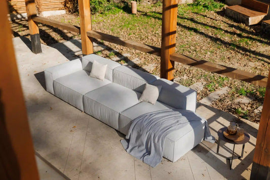 Gray modular sofa with cushions on a patio area with wooden beams and grass.