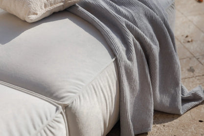 Light gray textured blanket draped over a beige cushion on a stone surface