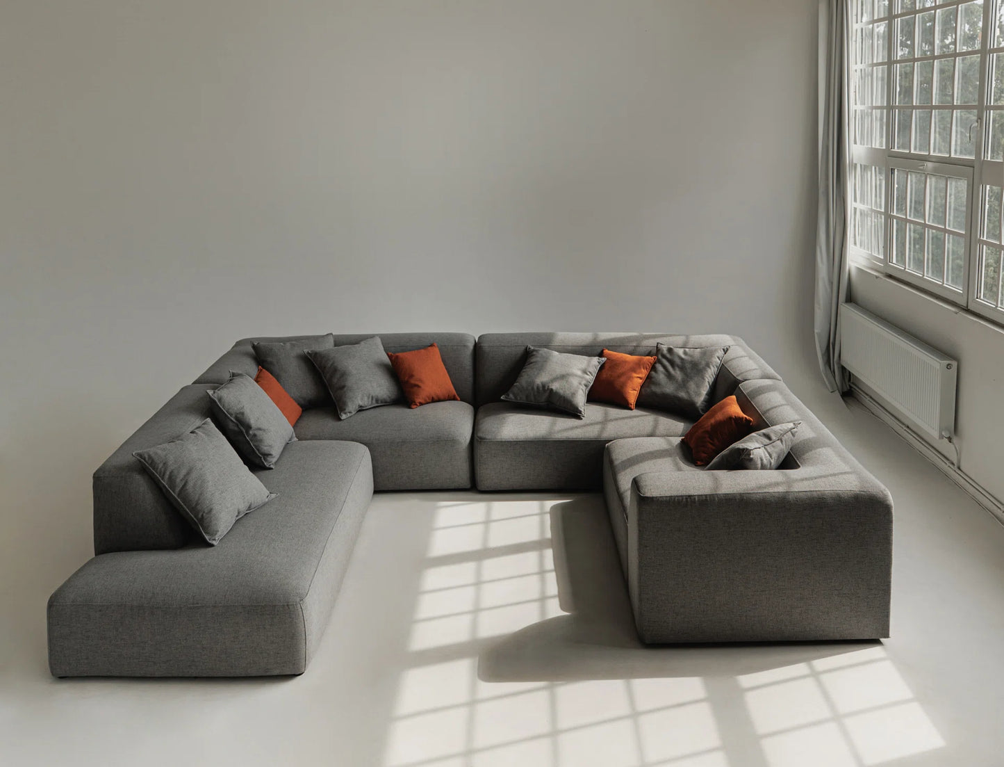 Gray sectional sofa with orange and gray cushions in a room with large windows.