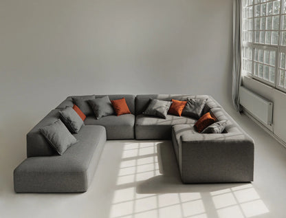 Gray sectional sofa with orange and gray cushions in a room with large windows.