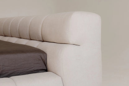 Close-up of a beige upholstered headboard with a pillow on a neutral background