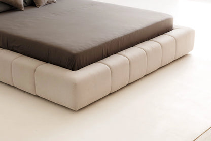 Beige upholstered bed frame with a brown mattress on a light beige floor.