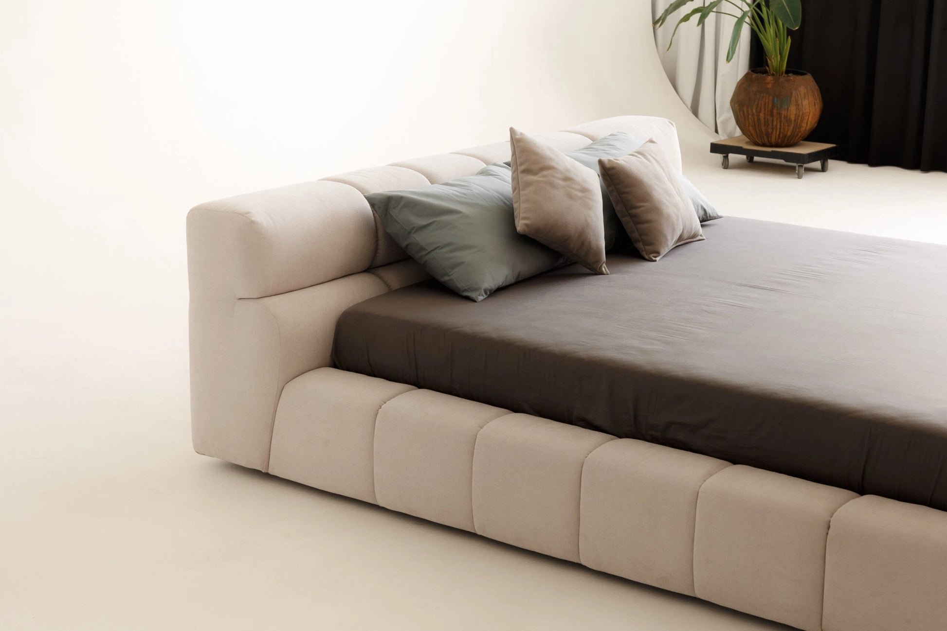 Beige sofa with a brown mattress and decorative pillows in a minimalistic room.