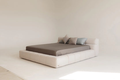 Modern bed with beige frame and gray mattress in a minimalistic room.