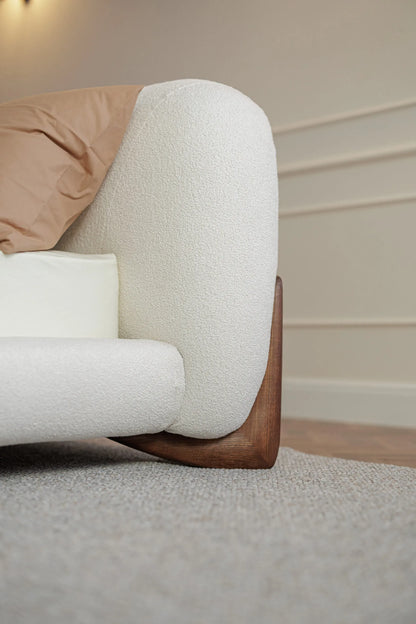 Corner of a modern bed with in white boucle and with wooden designer legs.