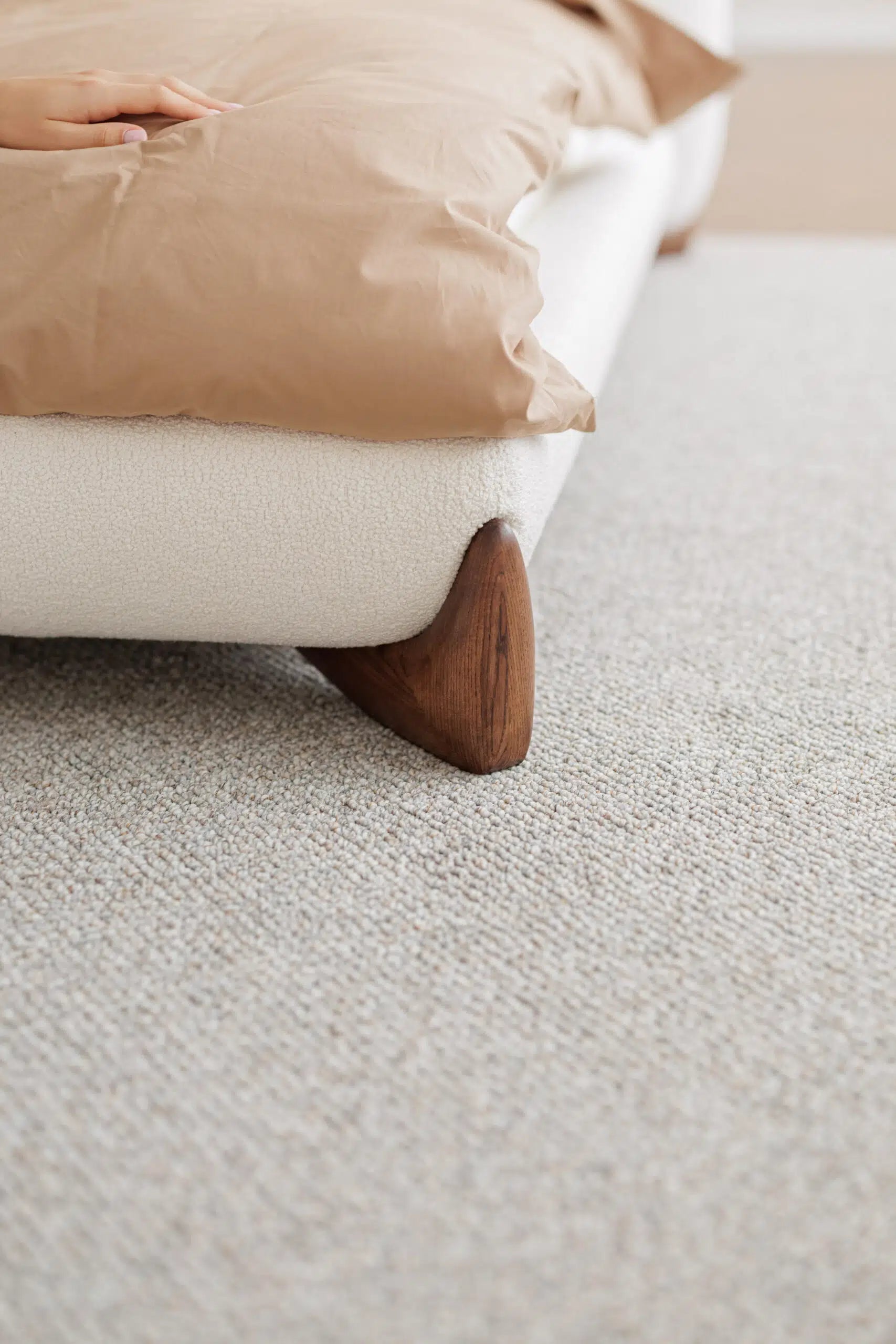 Close-up of a wooden legs of white luxury bed on a textured carpet