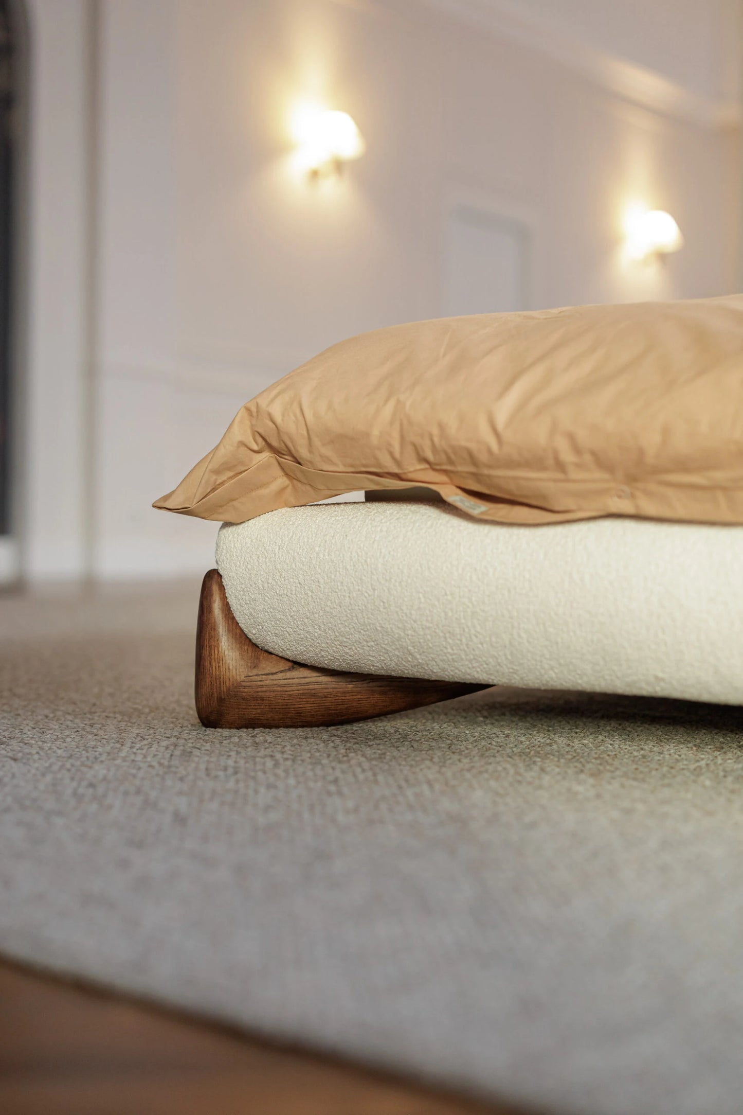 Close-up of a white boucle bed with wooden feet, blurred background
