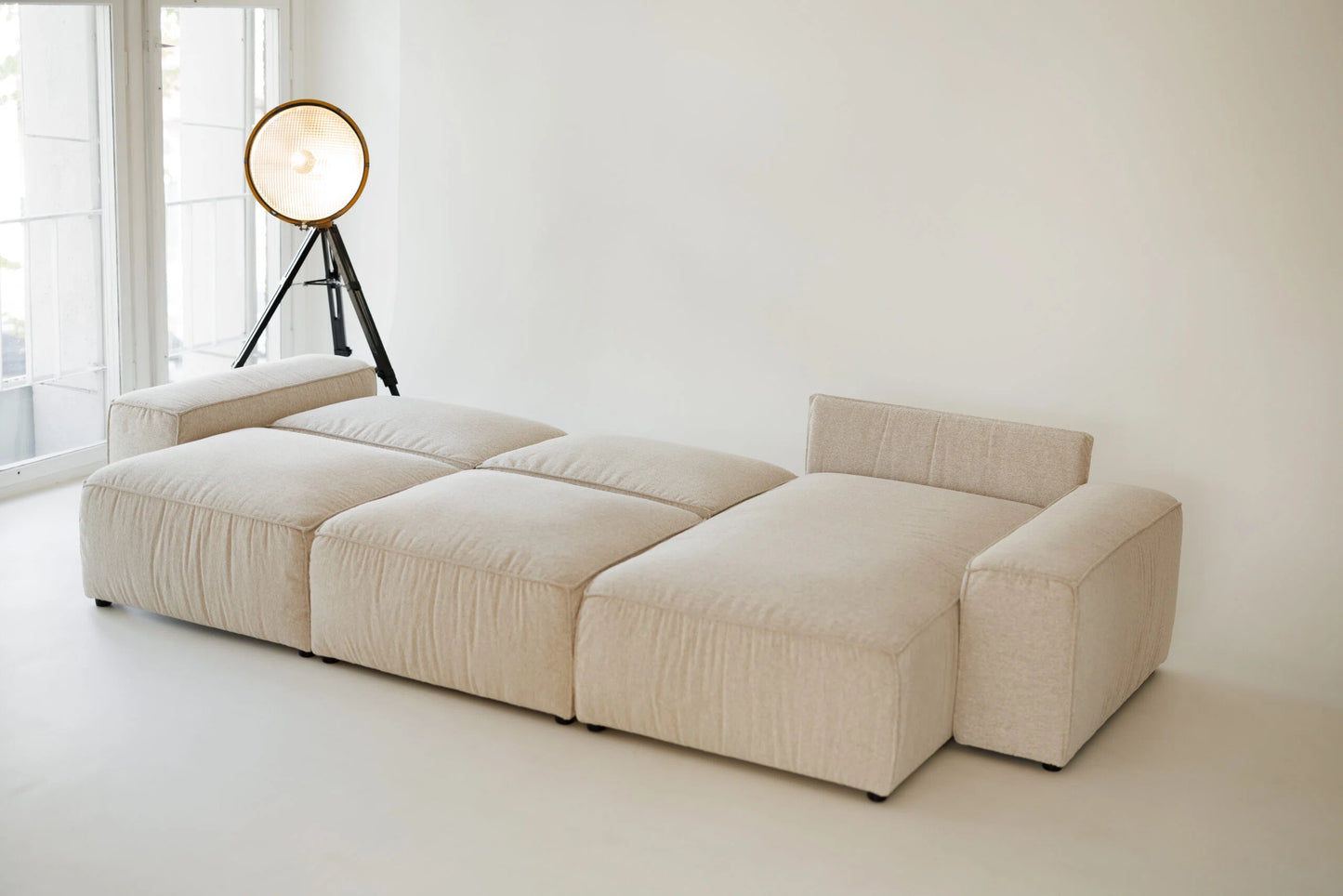 Beige sectional sofa  bed in a minimalistic room with a lamp.