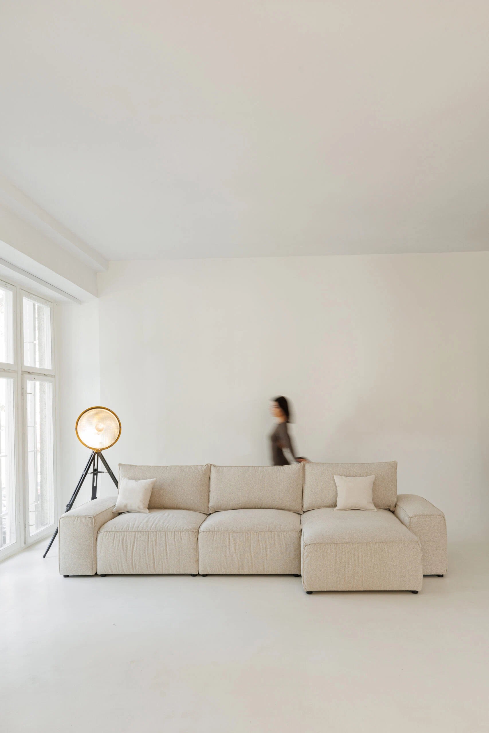 Beige sectional sofa bed in a minimalistic room with a person in the background.