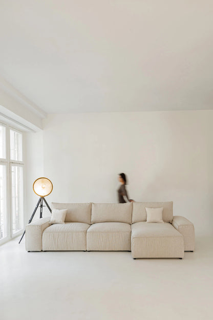 Beige sectional sofa bed in a minimalistic room with a person in the background.