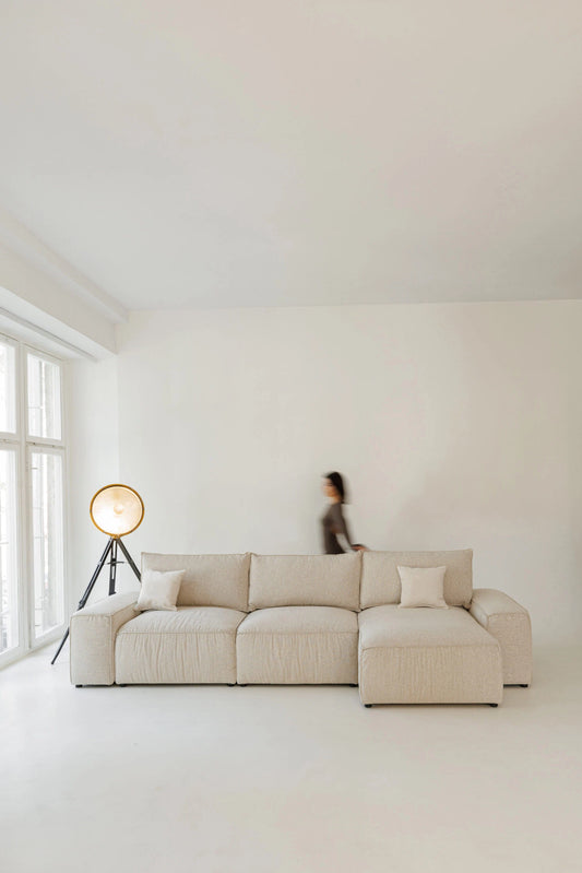 Beige sectional sofa bed in a minimalistic room with a person in the background.