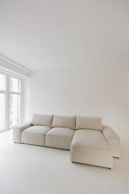 Beige sectional sofa bed in a minimalistic room with white walls and floor.