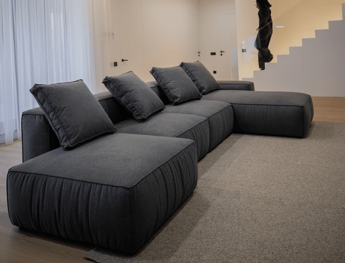 Gray sectional modular sofa in a modern living room setting with a staircase in the background.