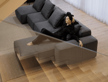 Woman lying on a modern gray sectional sofa in a minimalistic room.