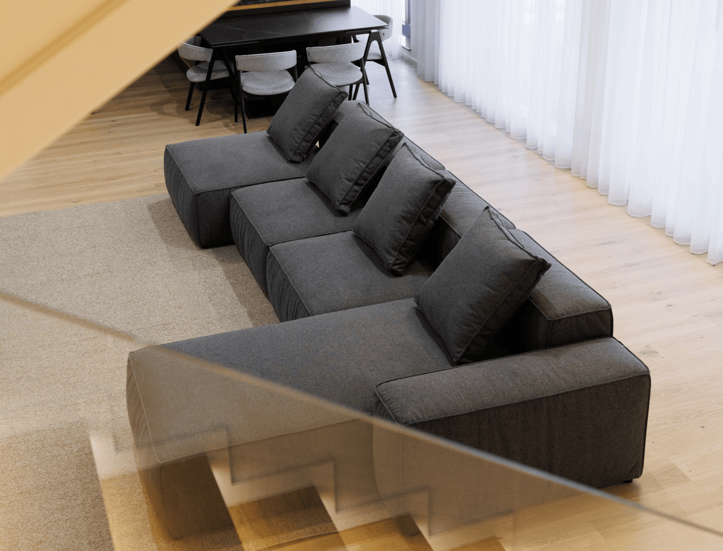 Black sectional sofa in a modern living room with a dining table in the background.