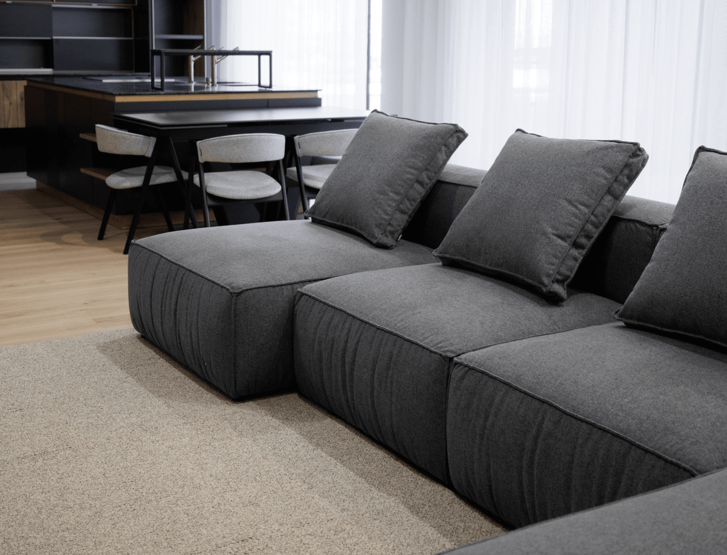 Gray sectional sofa in a modern living room with a kitchen in the background.