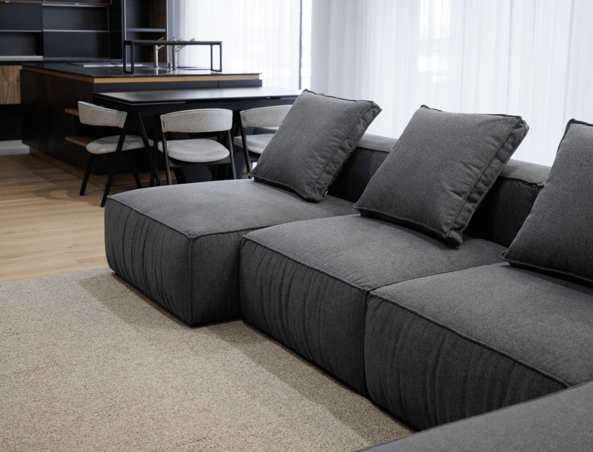 Gray sectional sofa in a modern living room with a kitchen in the background.