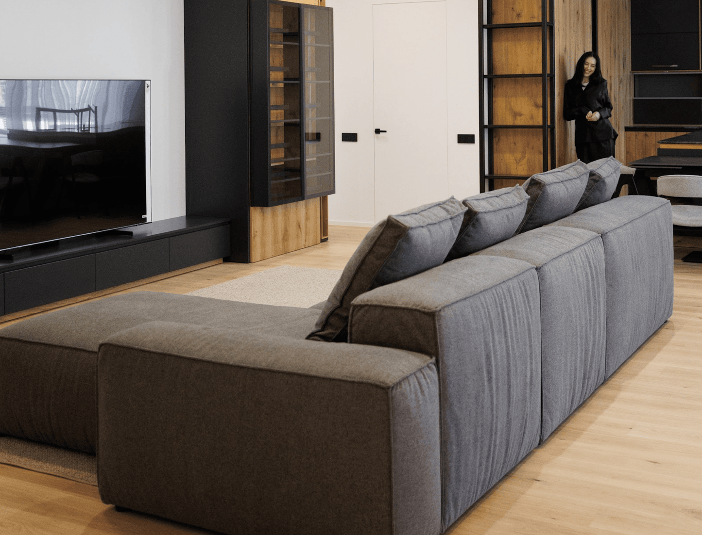 Black sectional sofa in a modern living room with a television and wooden floor.