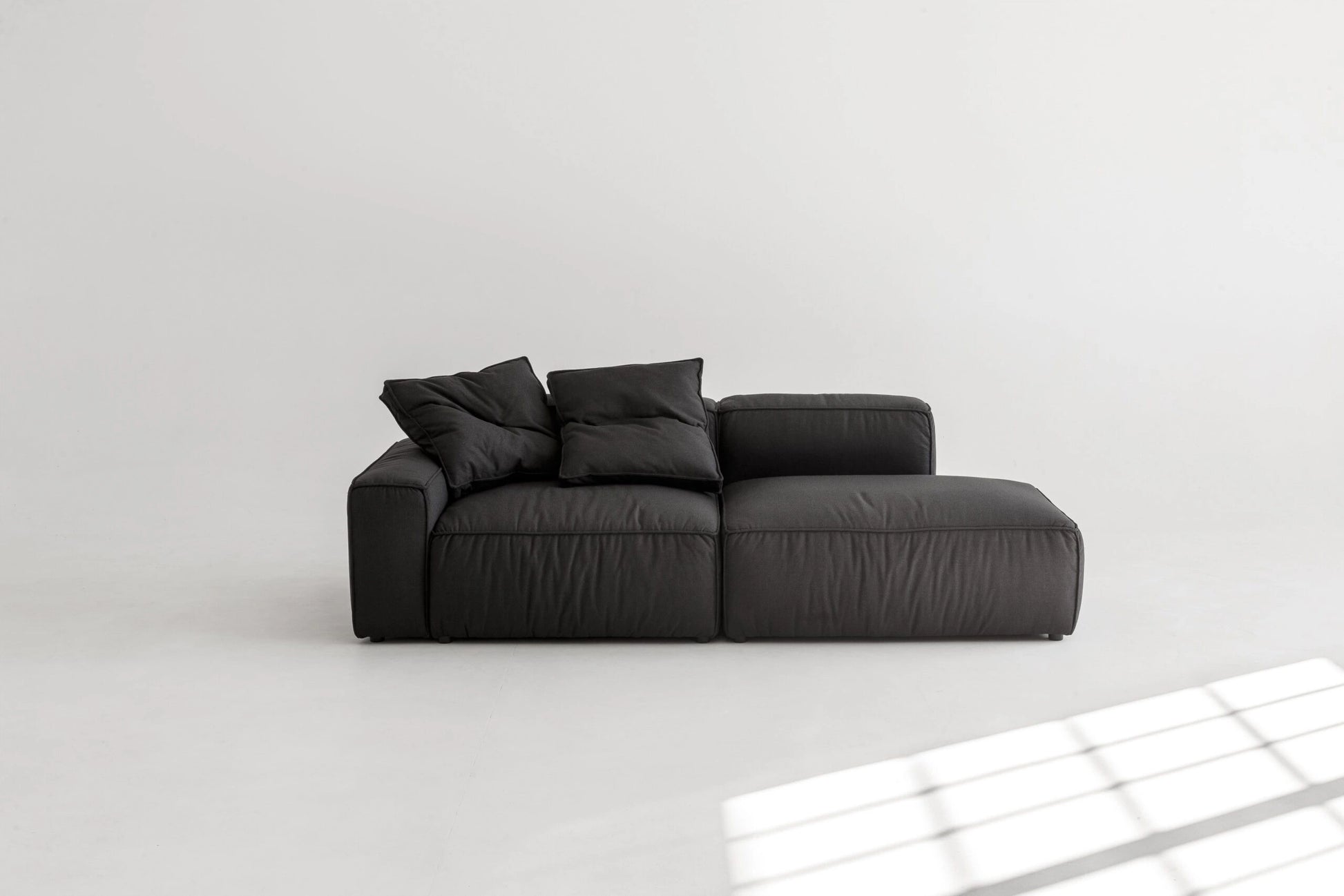 Black modular sofa on a white floor with a light gray wall