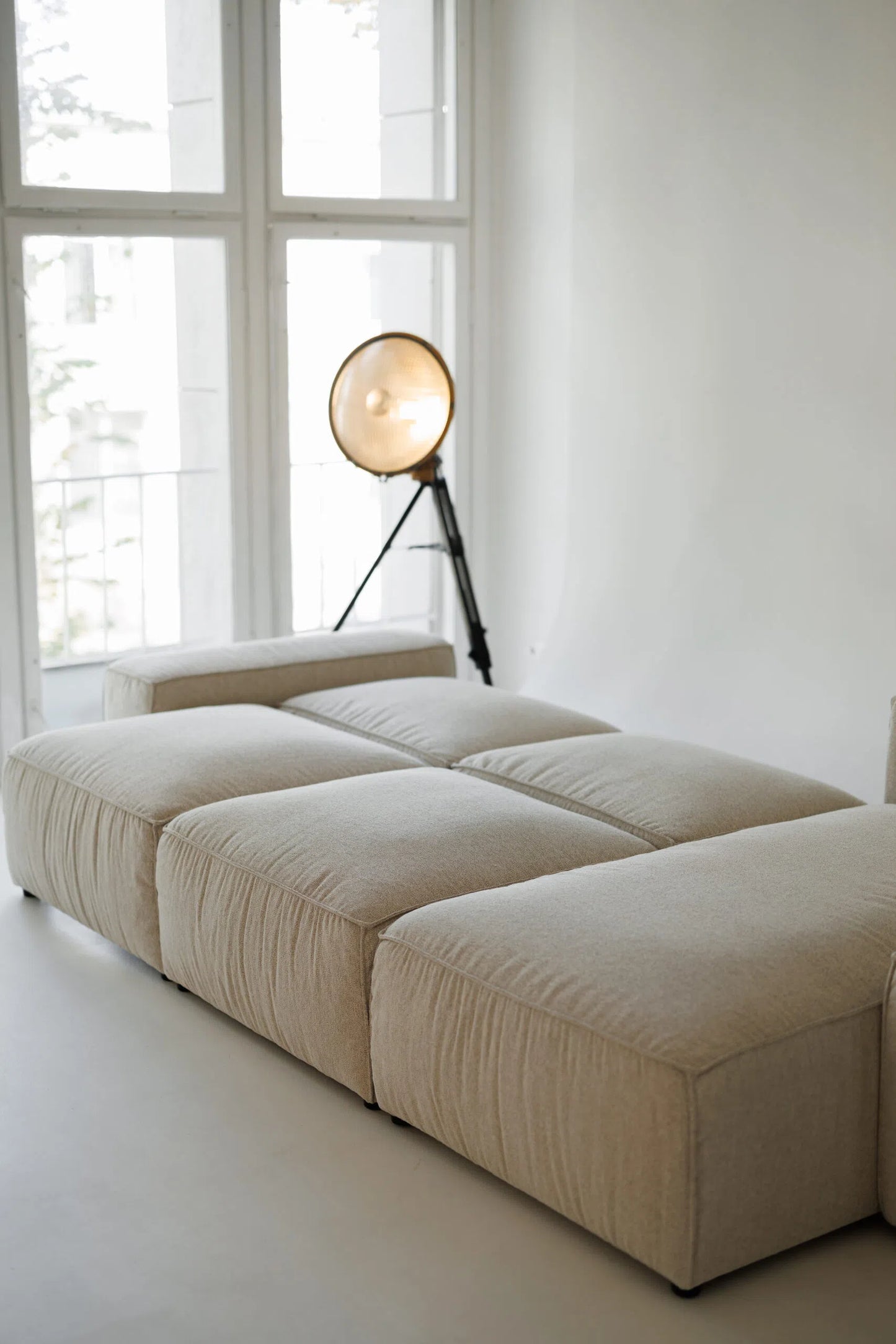 Beige sectional sofa bed  in a room with large windows and a floor lamp.