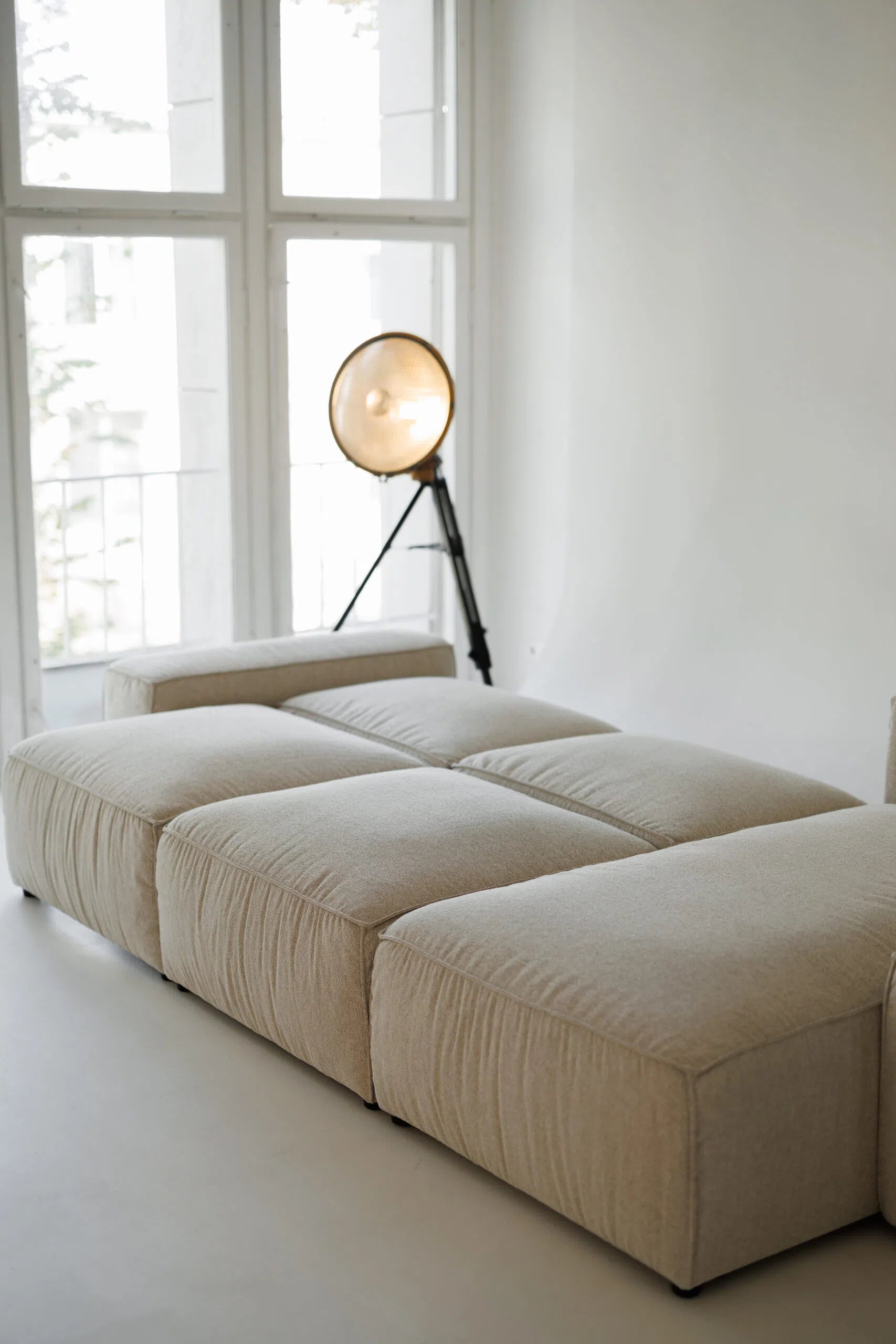 Beige sectional sofa bed  in a room with large windows and a floor lamp.