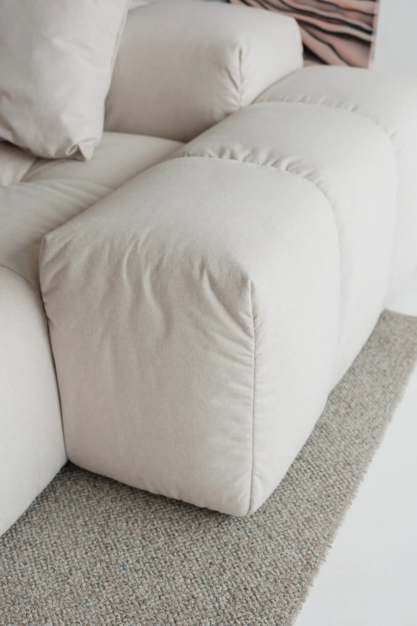 Close-up of a beige sofa with cushions on a light-colored floor.