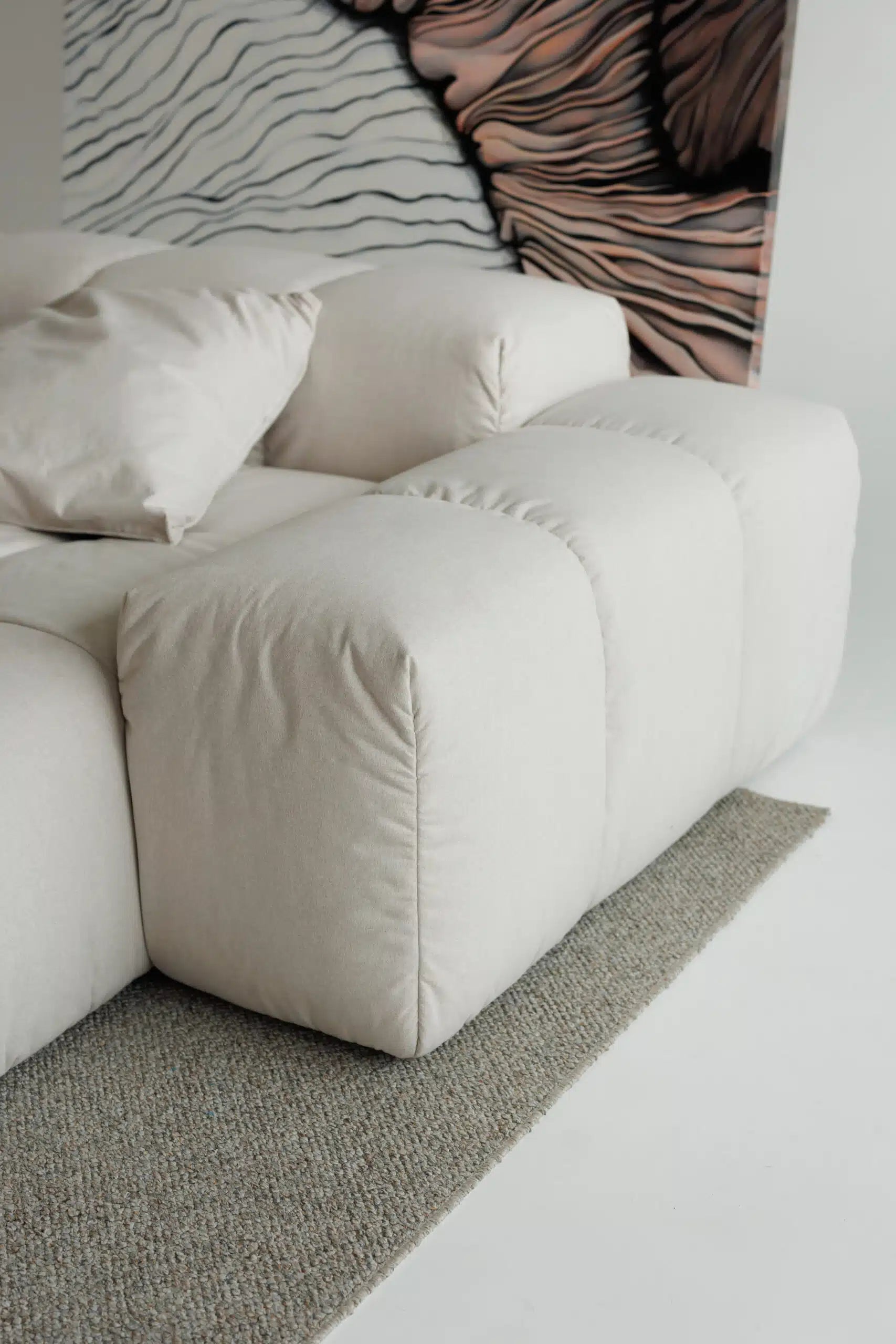Beige modular sofa with a textured wall and rug in a minimalistic room