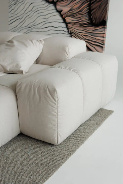 Beige modular sofa with a textured wall and rug in a minimalistic room