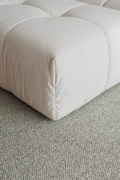 Close-up of a beige upholstered ottoman on a textured gray carpet
